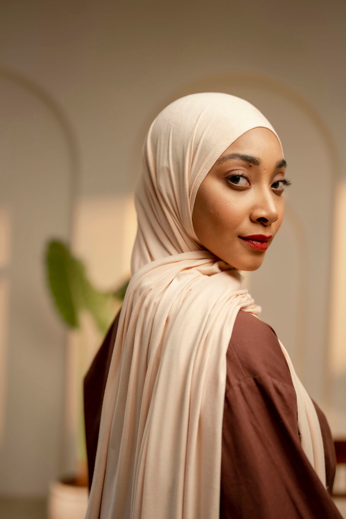 Woman wearing a beige hijab and brown top in an indoor setting