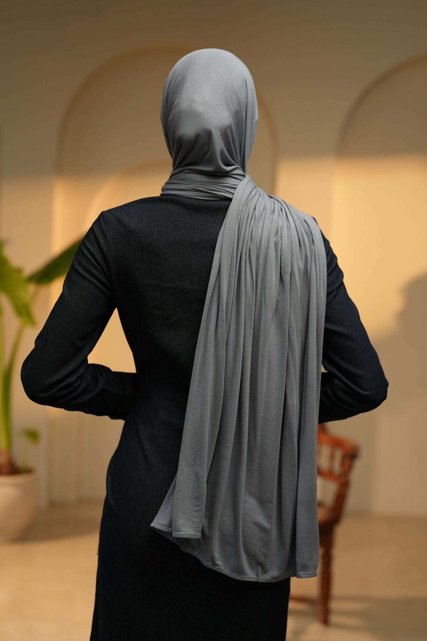 Woman wearing a light gray hijab in an indoor setting facing her back towards the camera