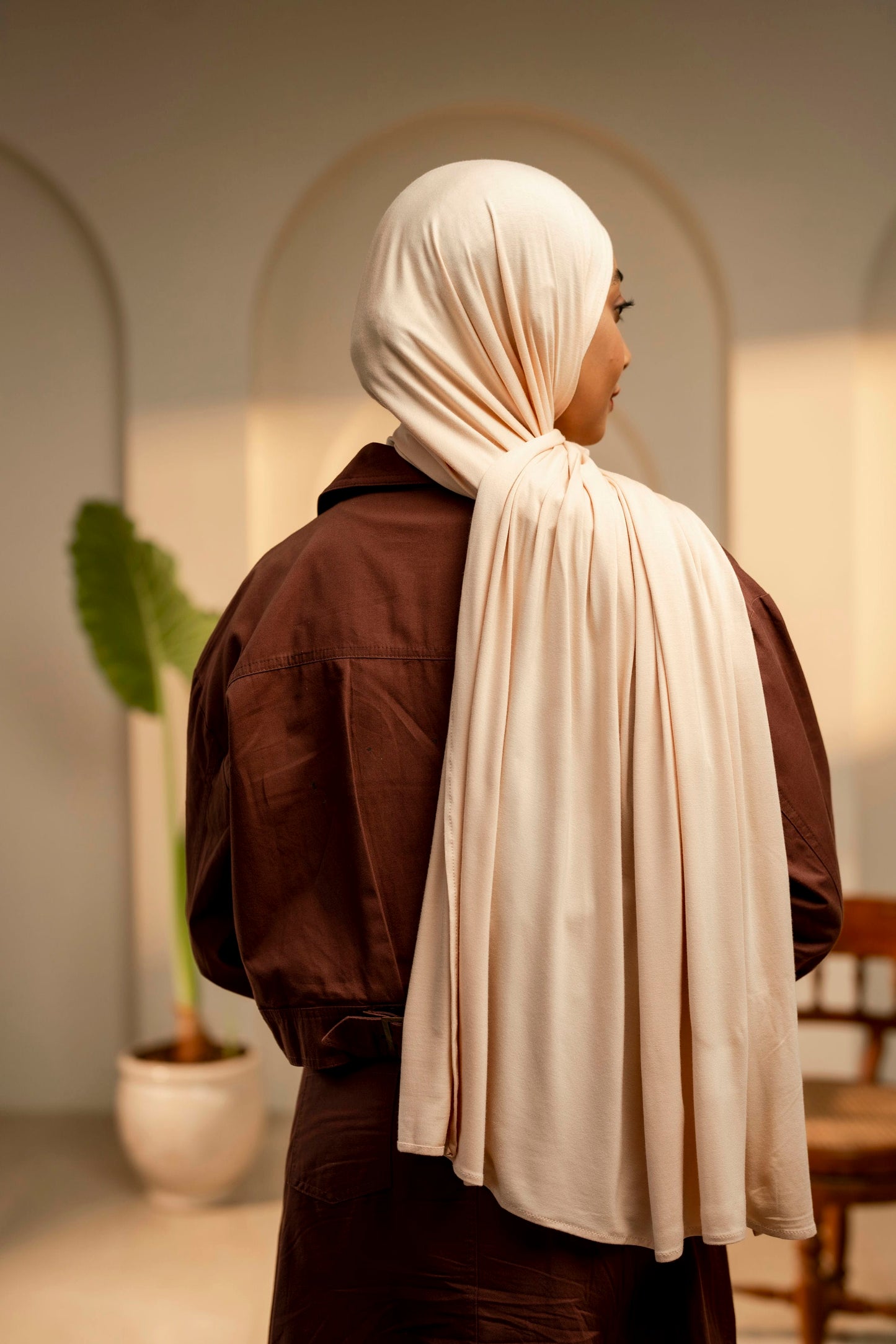 Person wearing a beige hijab and brown jacket in an indoor setting