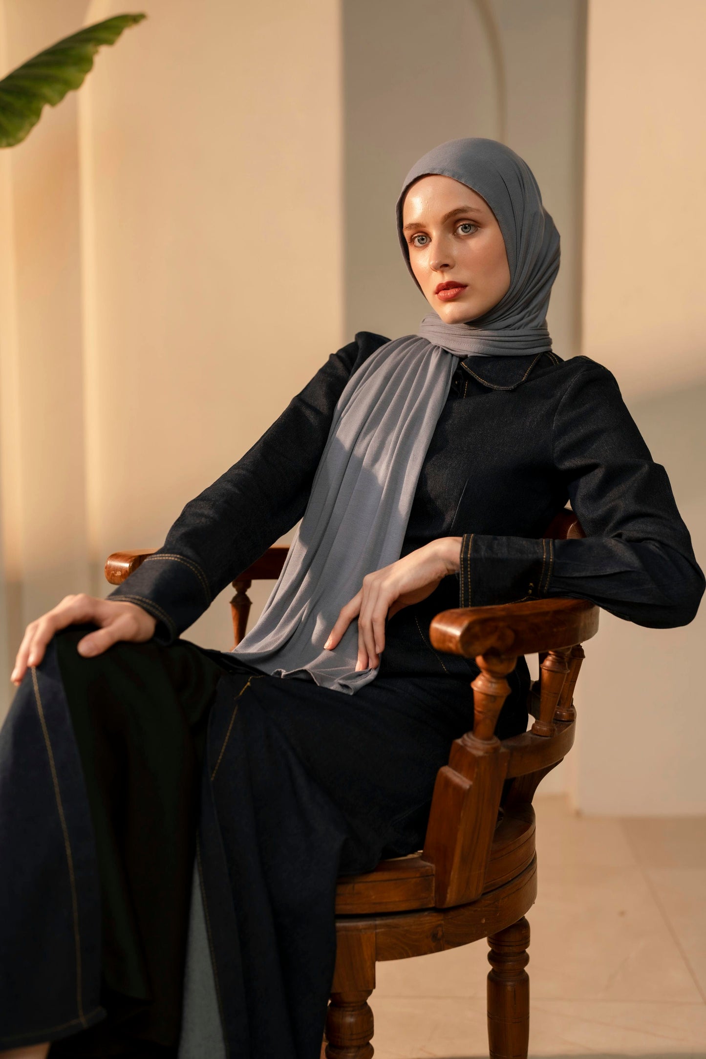 Woman wearing a light slate grey hijab and black outfit sitting on a wooden chair.
