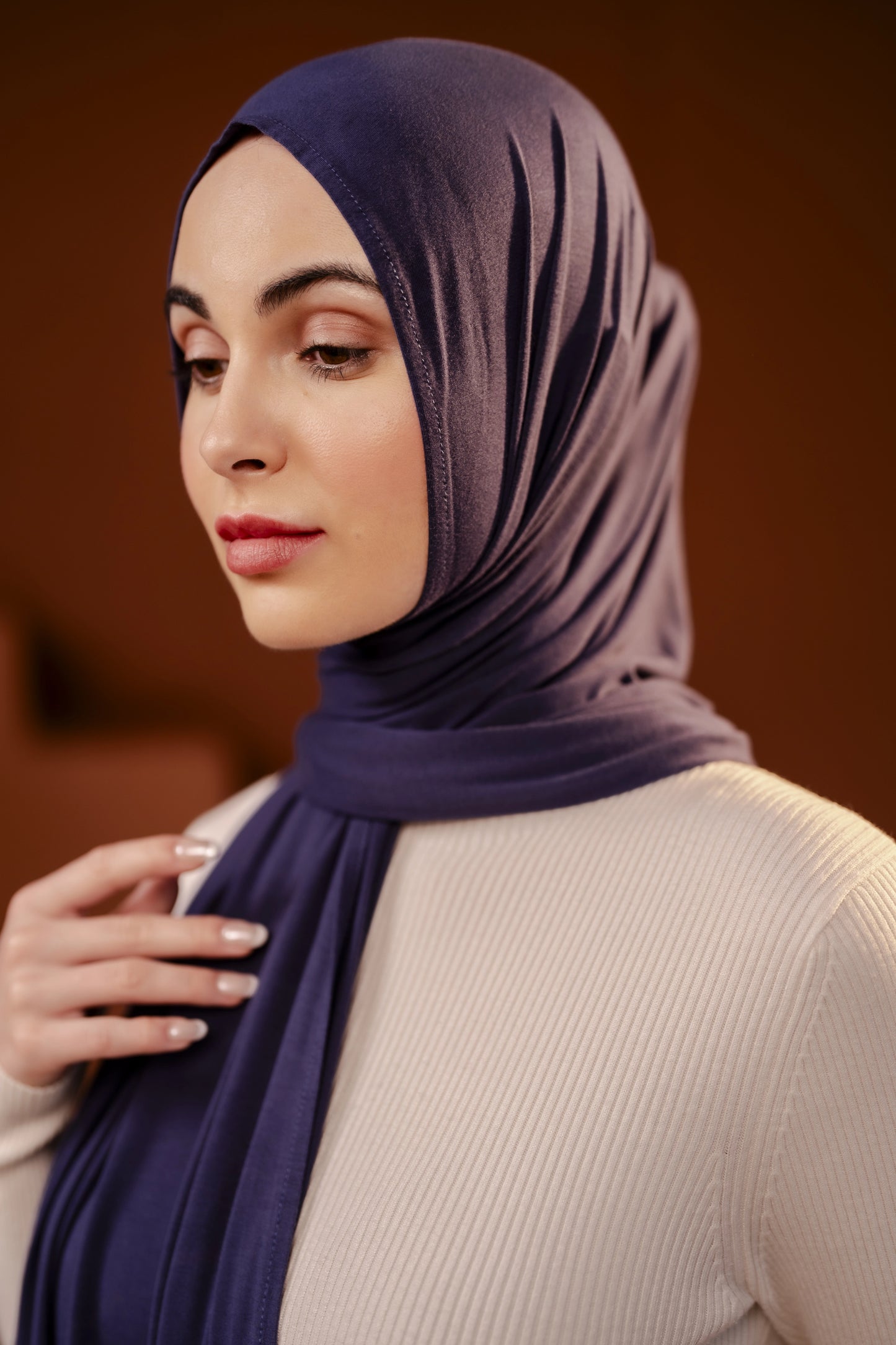 Woman wearing a dark purple hijab against a brown background