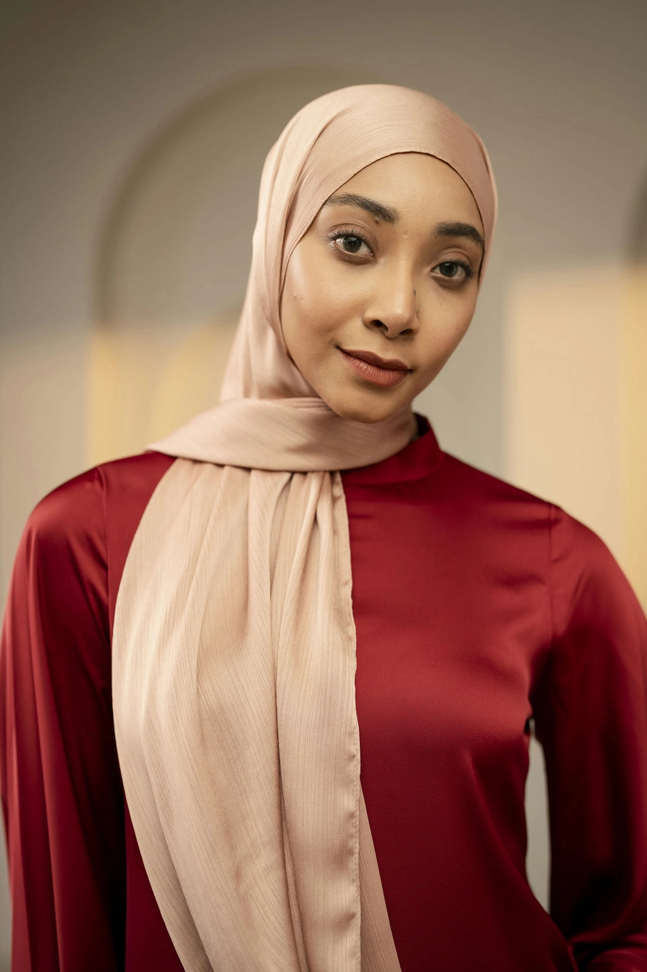Woman wearing a beige copper hijab and maroon top against a neutral background