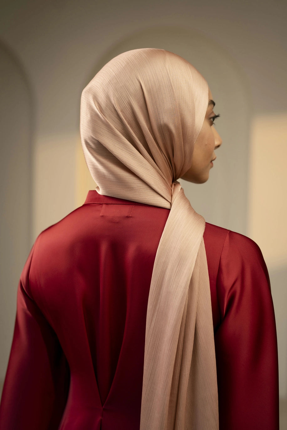 Woman wearing a beige hijab and maroon garment against a neutral background - copper