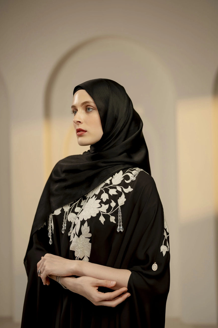 Woman wearing a black hijab with white embroidery in an indoor setting