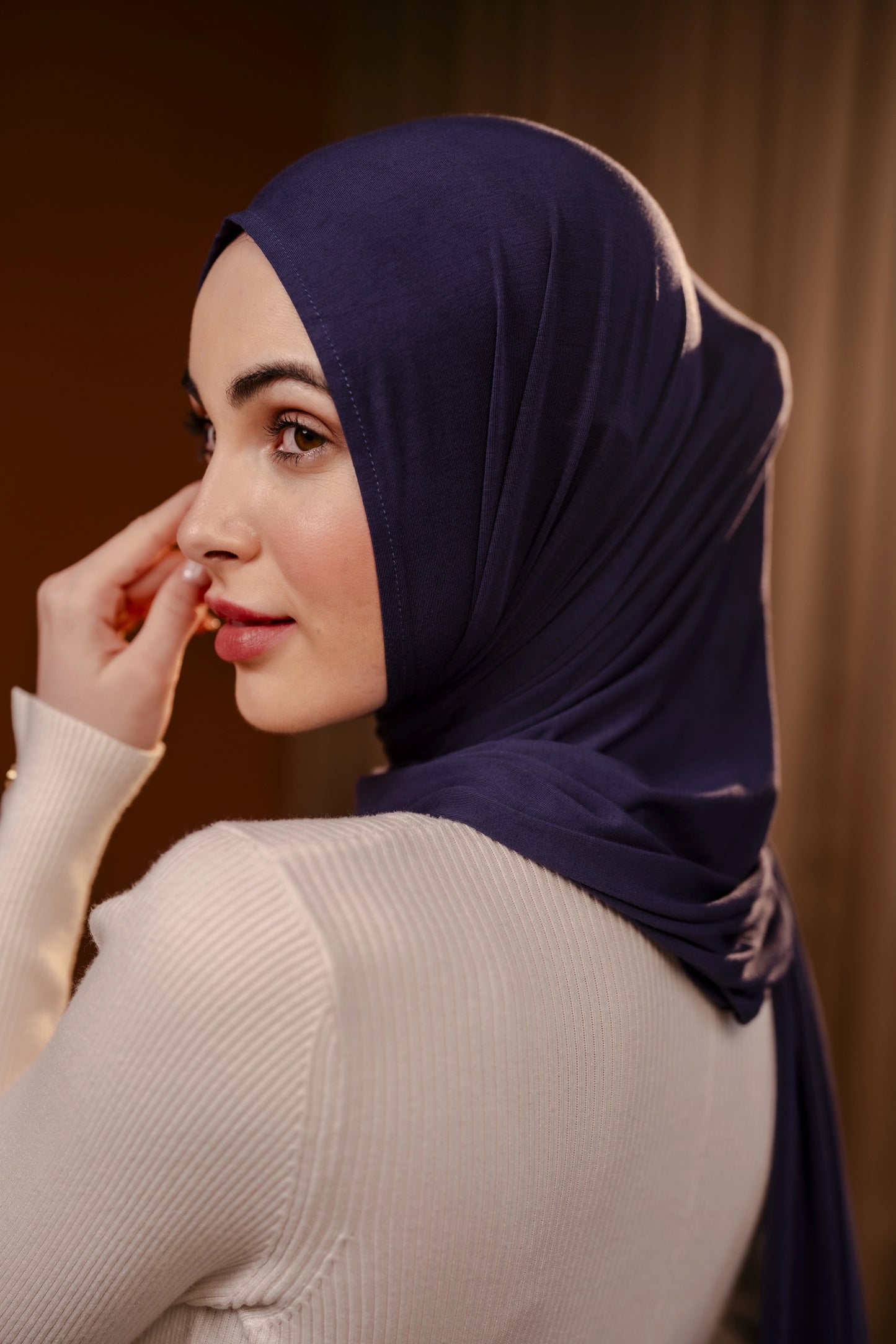 Woman wearing a dark blue hijab against a brown background