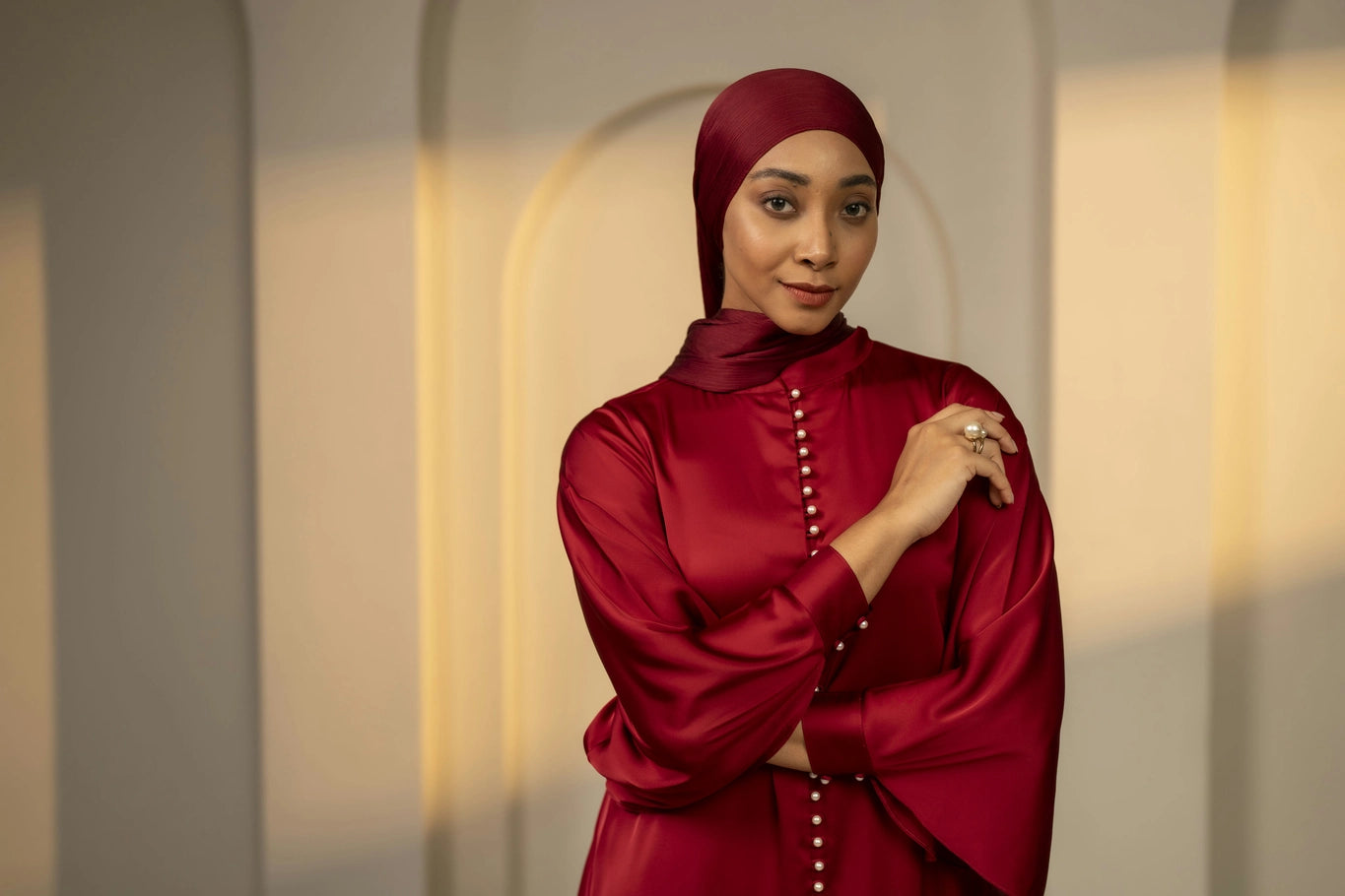 Woman wearing a red outfit with a matching headscarf against a neutral background