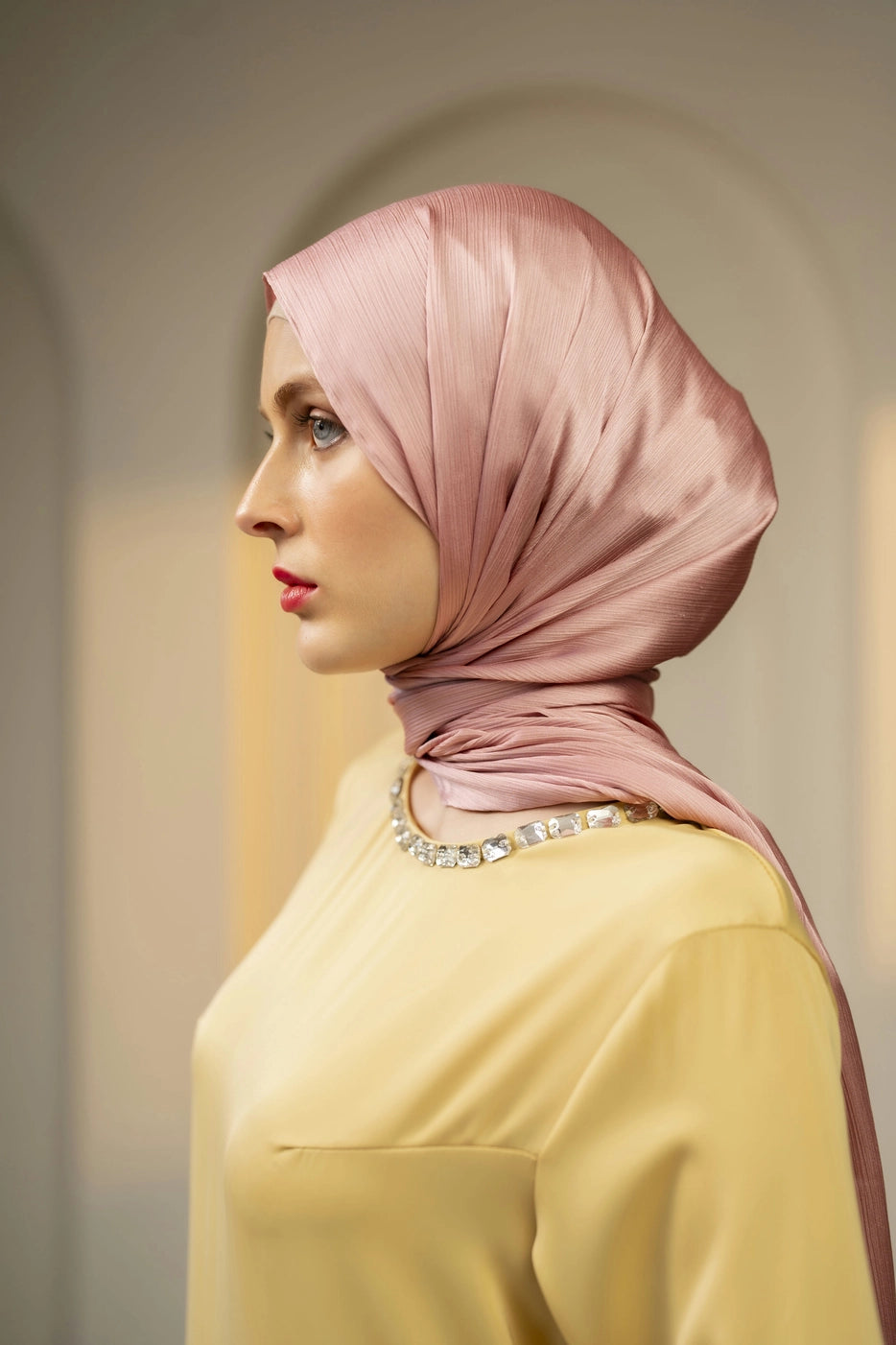 Woman wearing a pink hijab and yellow top against a neutral background