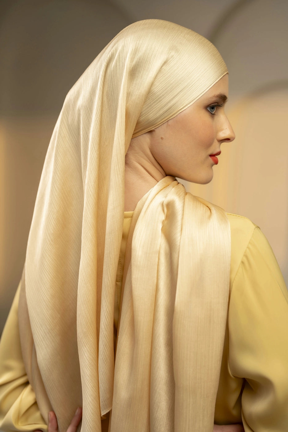 Woman wearing a ivory hijab and yellow top against a neutral background