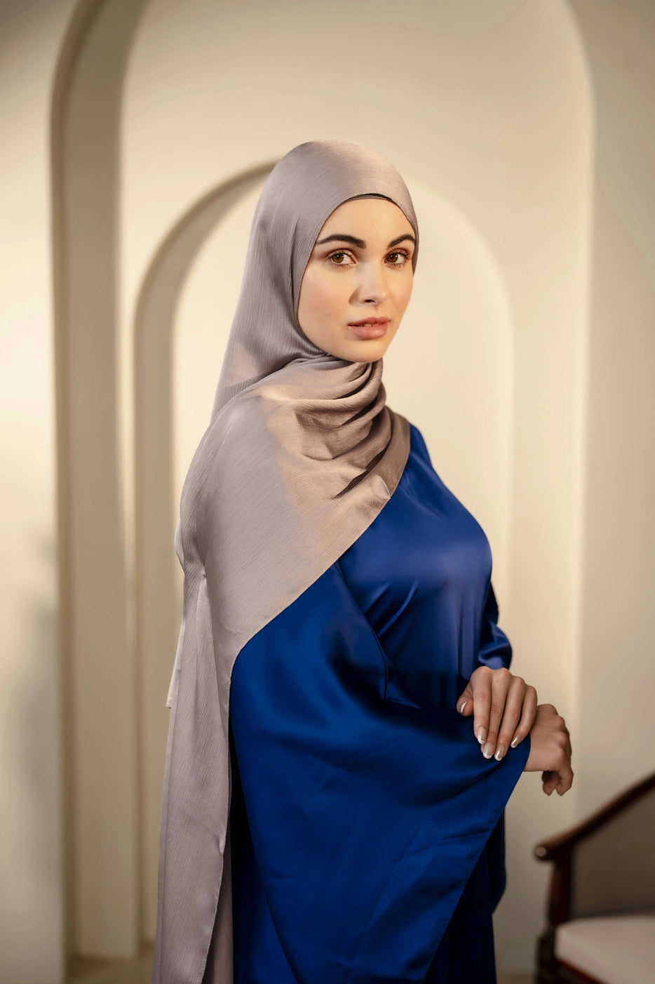Woman wearing a silver gray hijab and dark navy dress standing in an archway.
