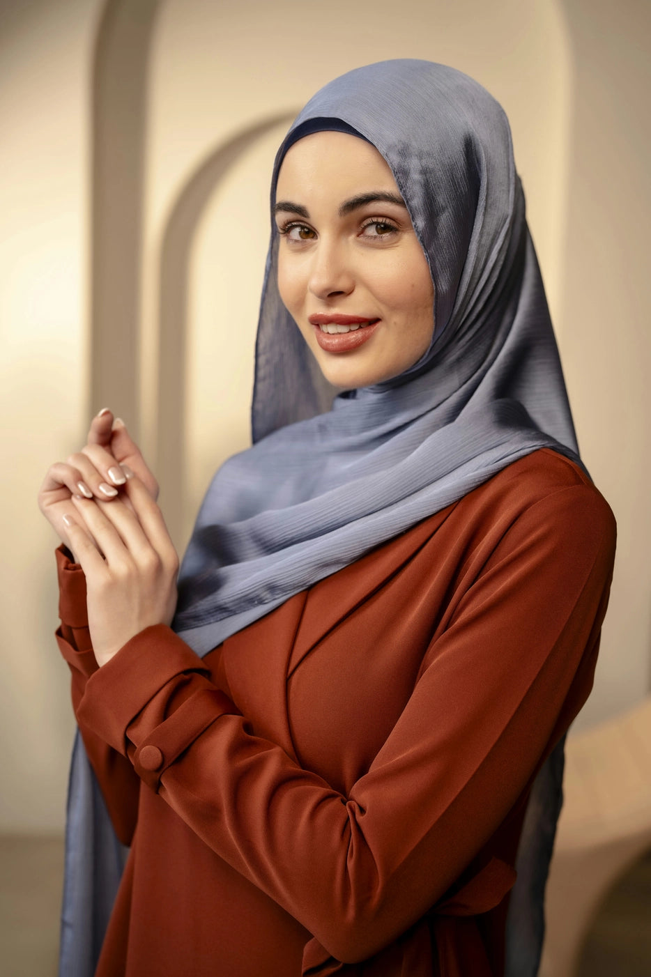 Woman wearing a blue hijab and brown top against a neutral background