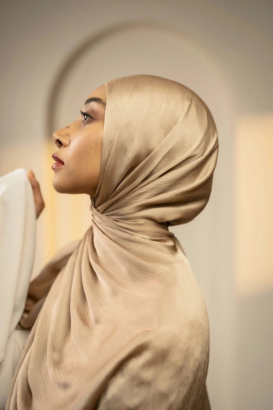 Woman wearing a gold hijab against a neutral background