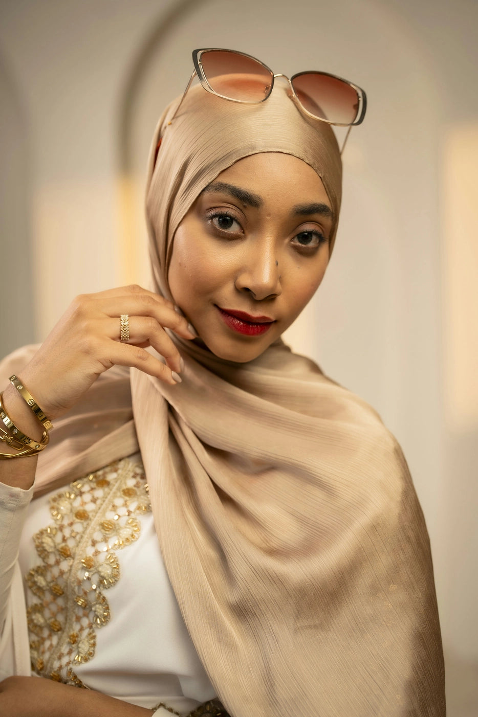 Woman wearing a beige gold hijab with sunglasses on her head, posing indoors.