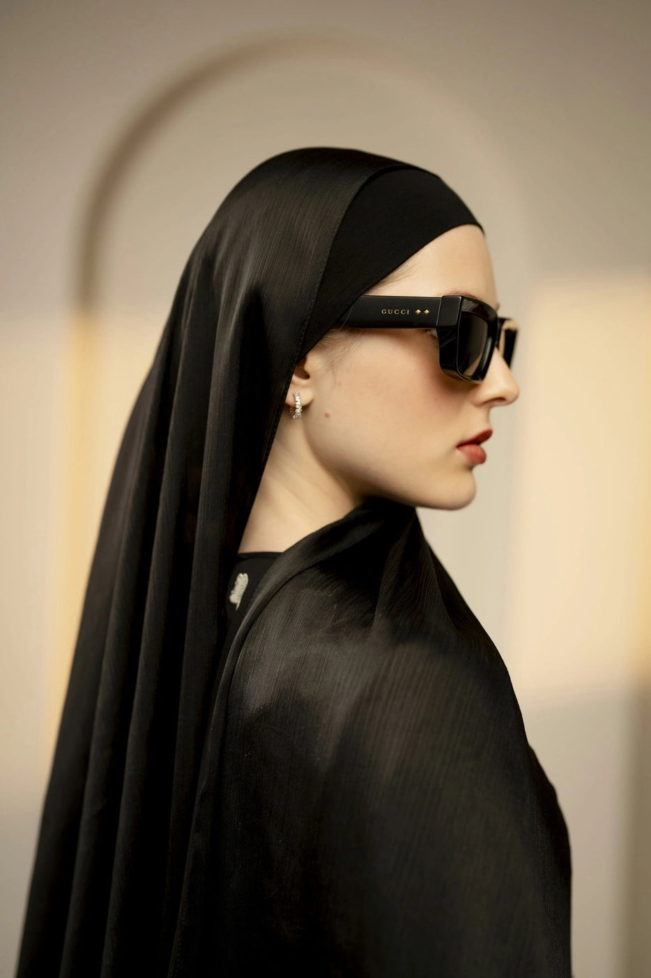 Person wearing a black textured silk hijab and sunglasses with a blurred background