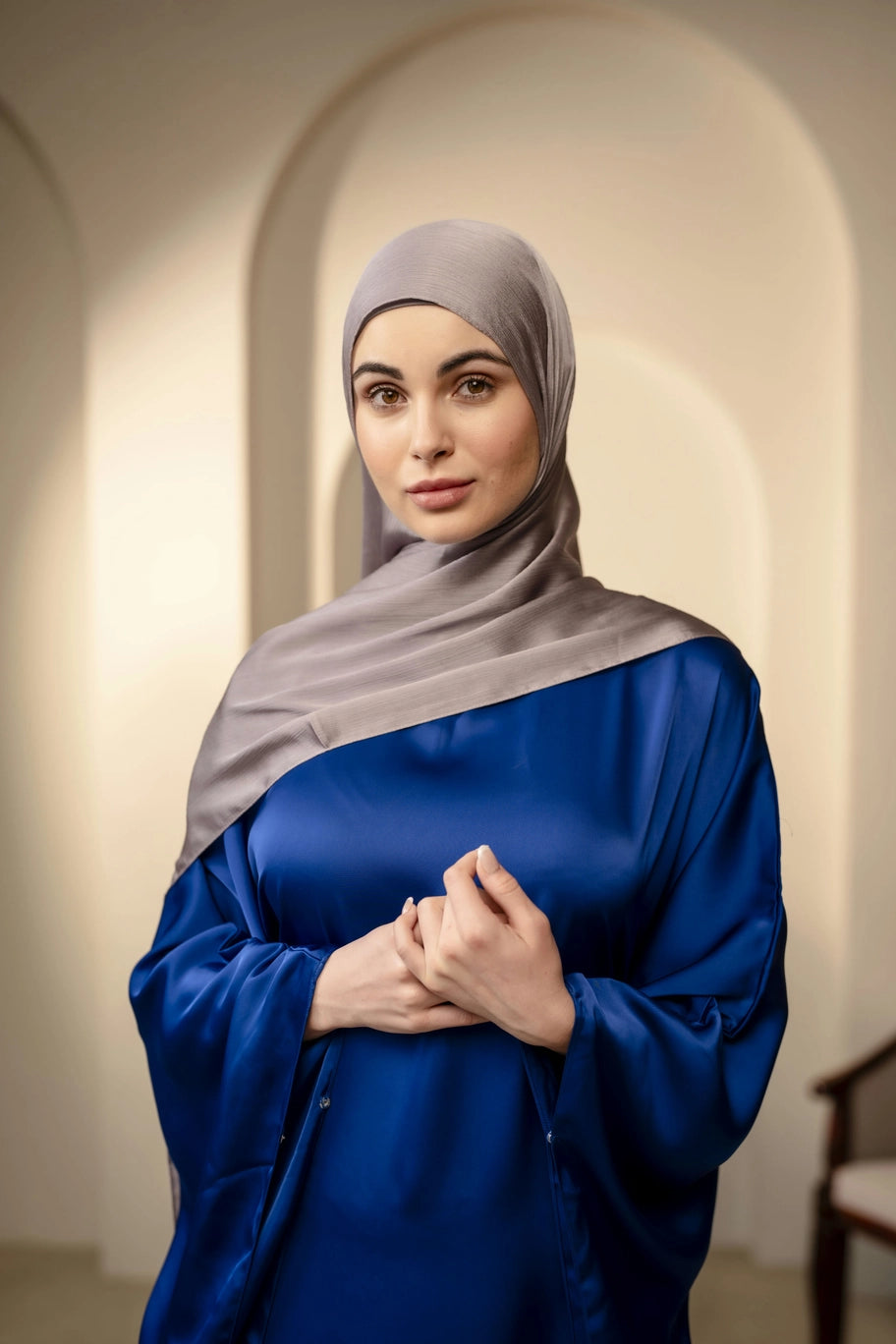 Woman wearing a navy top and silver gray hijab in an indoor setting