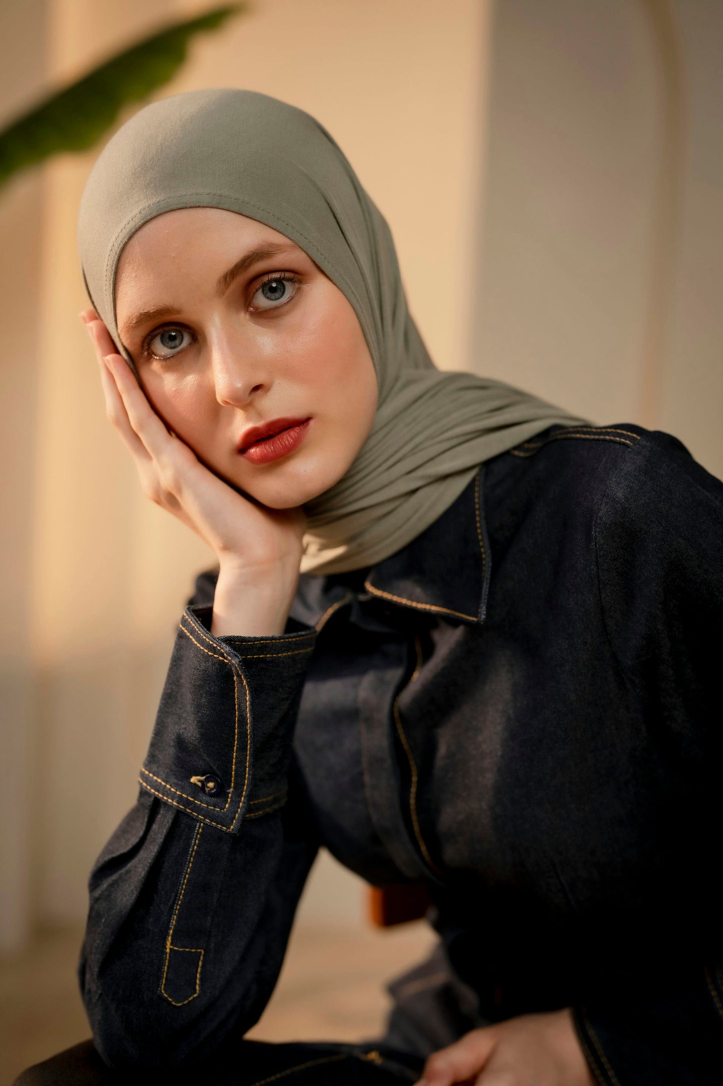 Woman wearing a green hijab with a blurred background resting her face on her palm