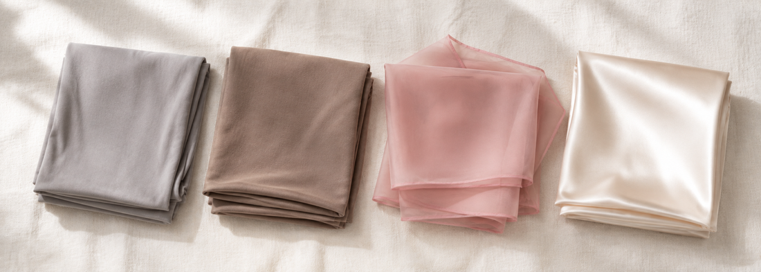 Four folded hijabs in modal, bamboo jersey, chiffon and satin laid side by side on a neutral background showing the different fabric weights and finishes — Hijab Elegance
