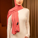 Woman wearing a pink hijab and white outfit against a dark curtain background