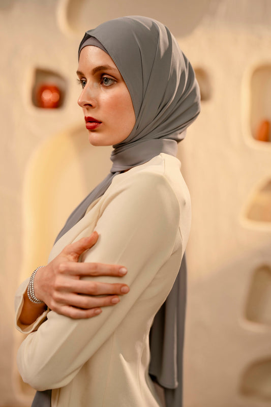 Woman wearing a gray hijab and beige outfit against a textured beige wall.