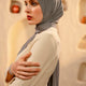 Woman wearing a gray hijab and beige outfit against a textured beige wall.