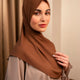 Woman wearing a brown hijab and beige outfit against a beige curtain background