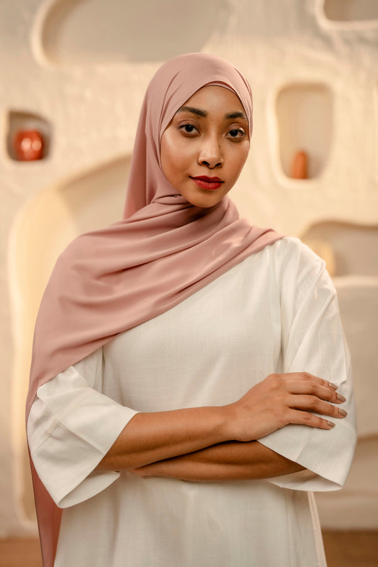 Woman wearing a pink hijab and white outfit in an abstract architectural setting - dusty pink