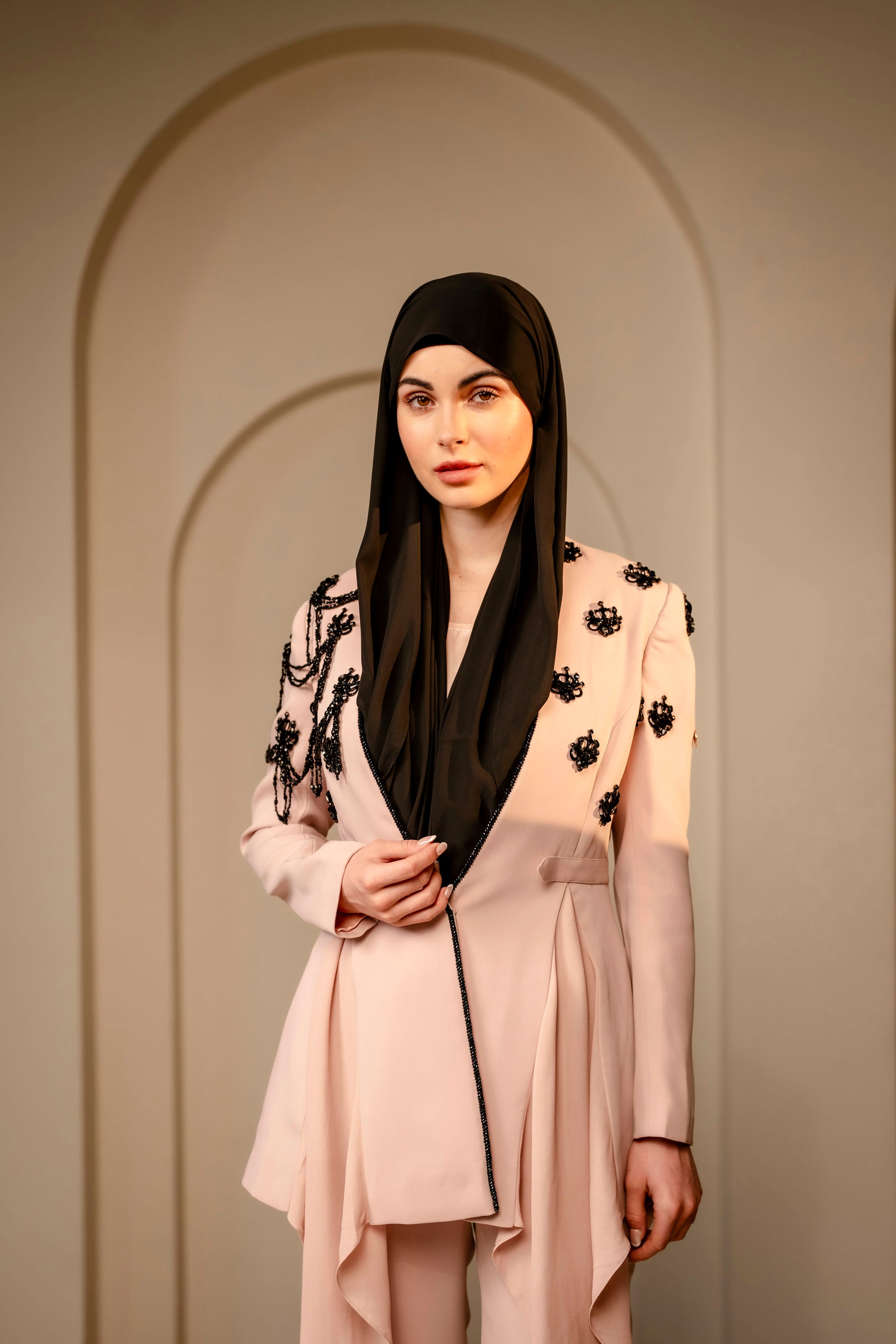 Woman wearing a beige outfit with black floral details against a neutral background