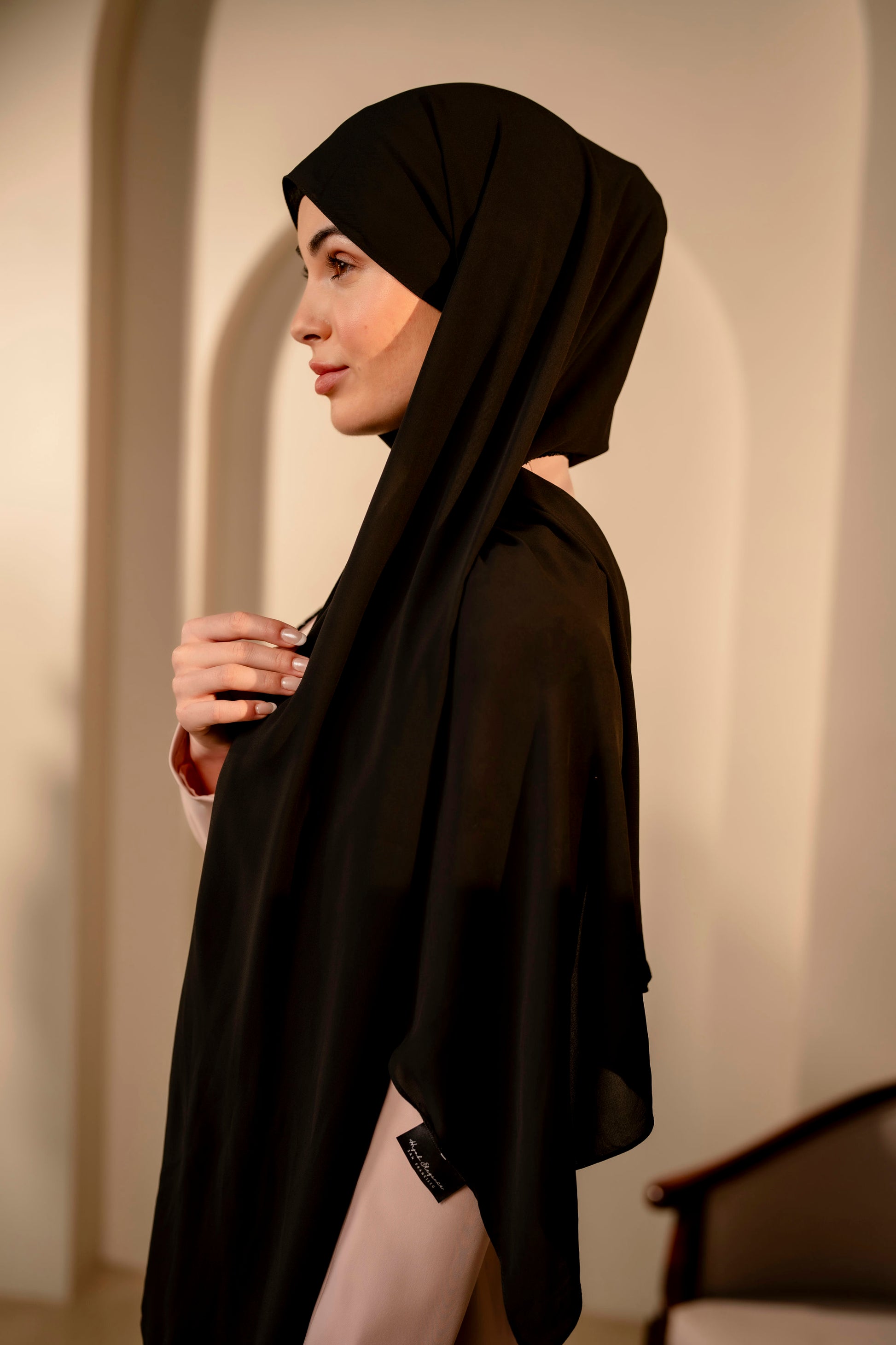 Woman wearing a black hijab and black outfit against a neutral background