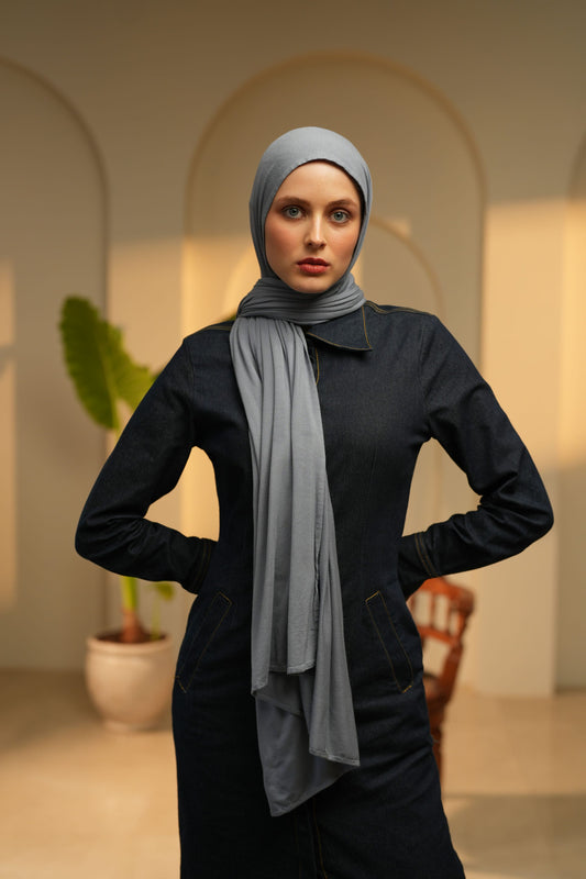 Person wearing a black outfit with a gray scarf and headscarf in an indoor setting.