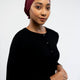 Woman wearing a dark cardigan and maroon headscarf on a light background