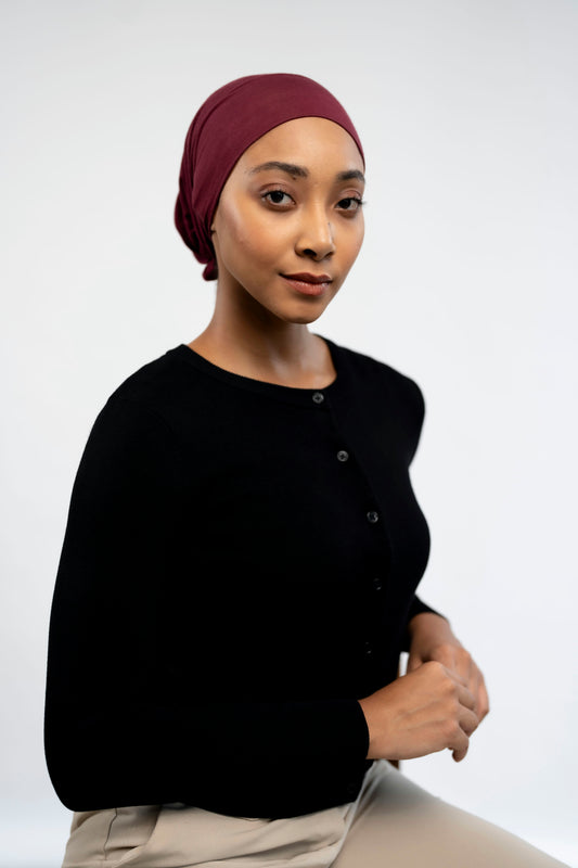 Woman wearing a dark cardigan and maroon headscarf on a light background