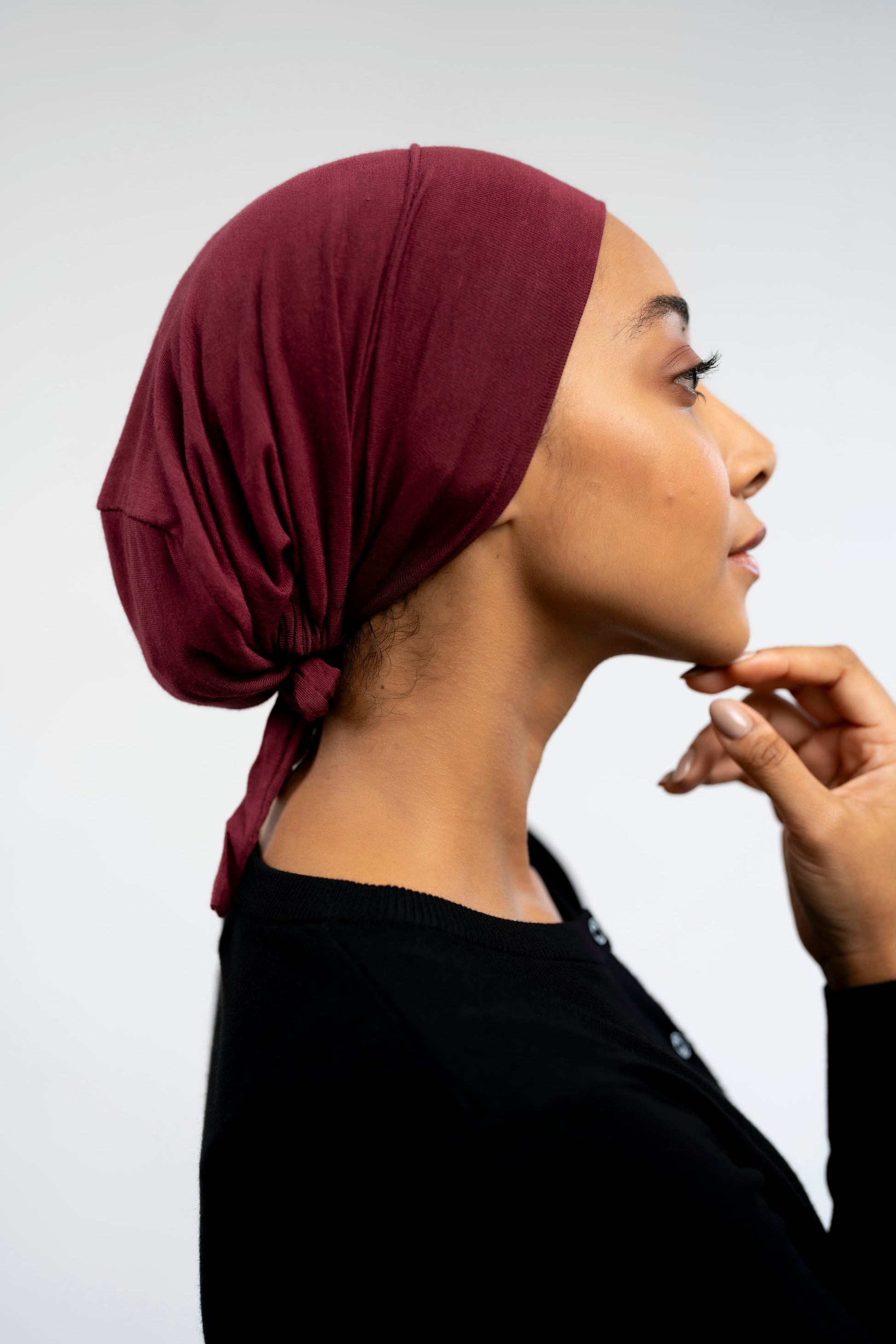 Woman wearing a burgundy headscarf against a light background - maroon