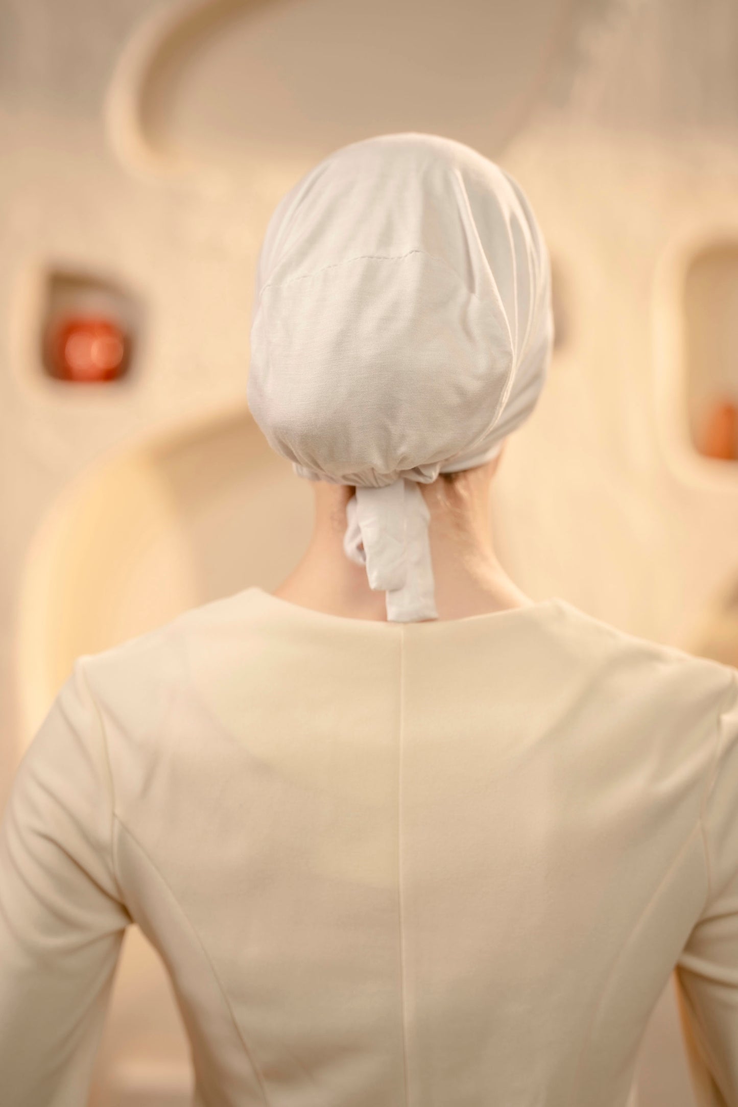 Person wearing a white hijab cap in a softly lit room.