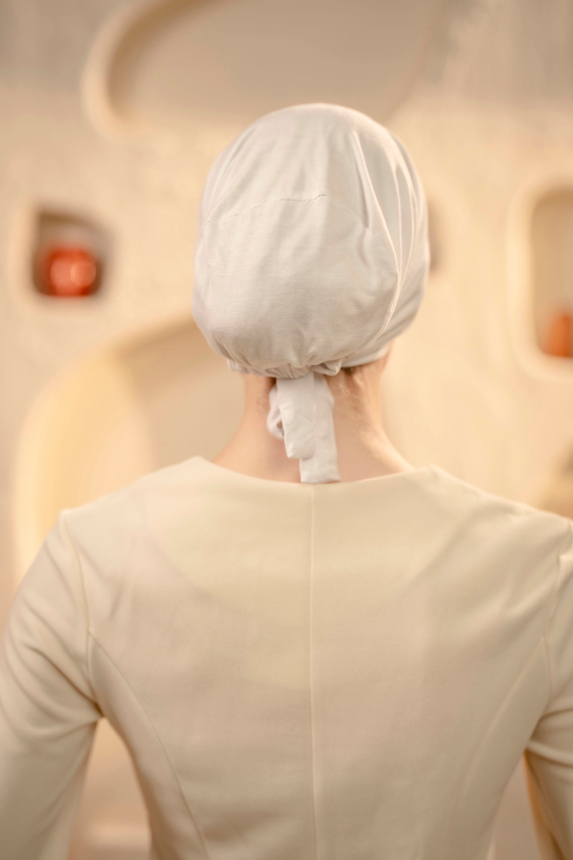 Person wearing a white hijab cap in a softly lit room.