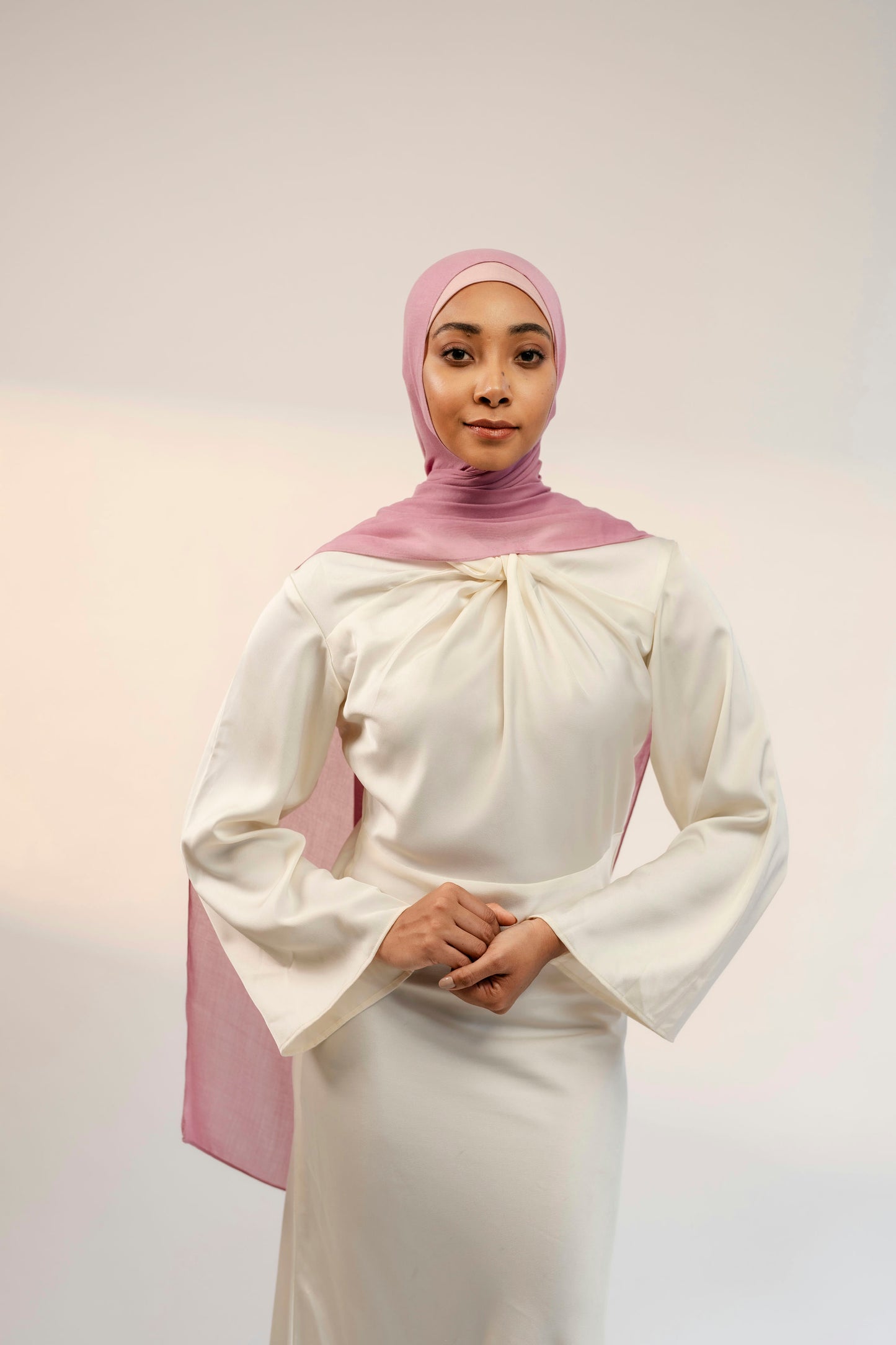 Woman wearing a white and pink outfit with a hijab on a plain background - cherry blossom