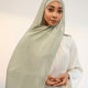 Woman wearing a light green headscarf and white outfit against a plain background 