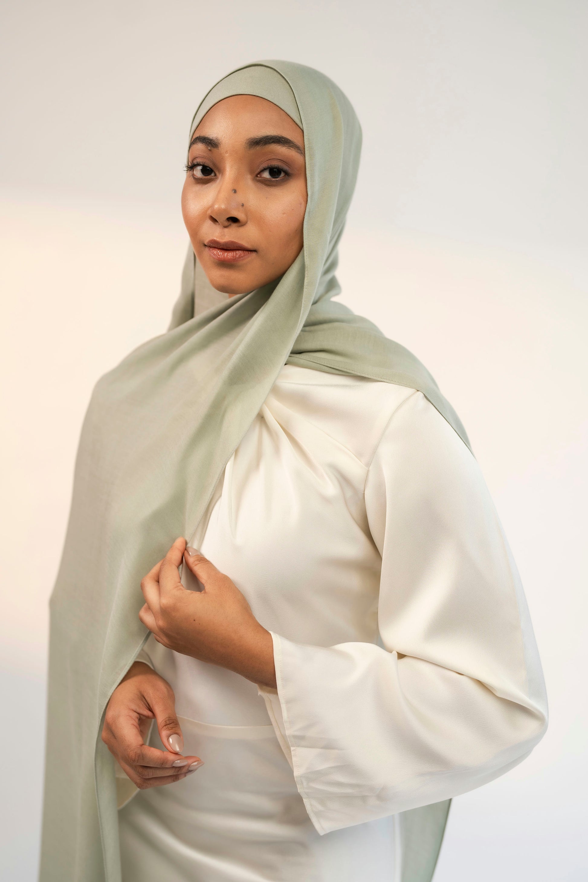 Woman wearing a light matcha green hijab and white outfit against a plain background