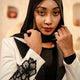 Woman wearing a black hijab and white jacket with floral design indoors.