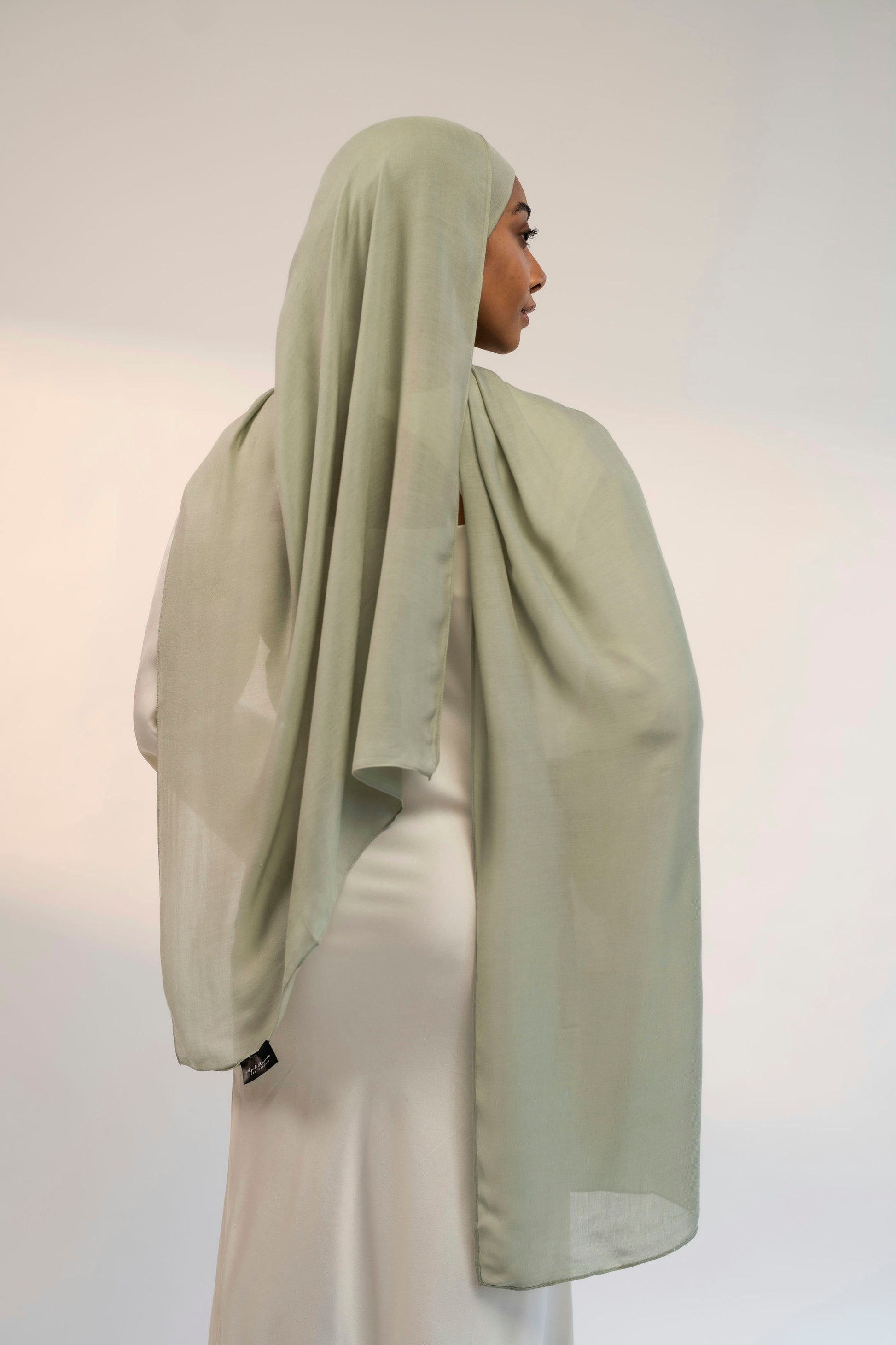 Person wearing a light green headscarf and white outfit against a plain background