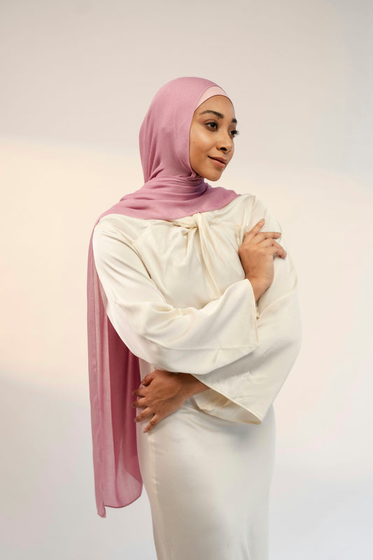 Woman wearing a white outfit and pink hijab against a plain background - cherry blossom