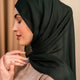 Woman wearing a dark hijab and beige top against a beige background - forest green
