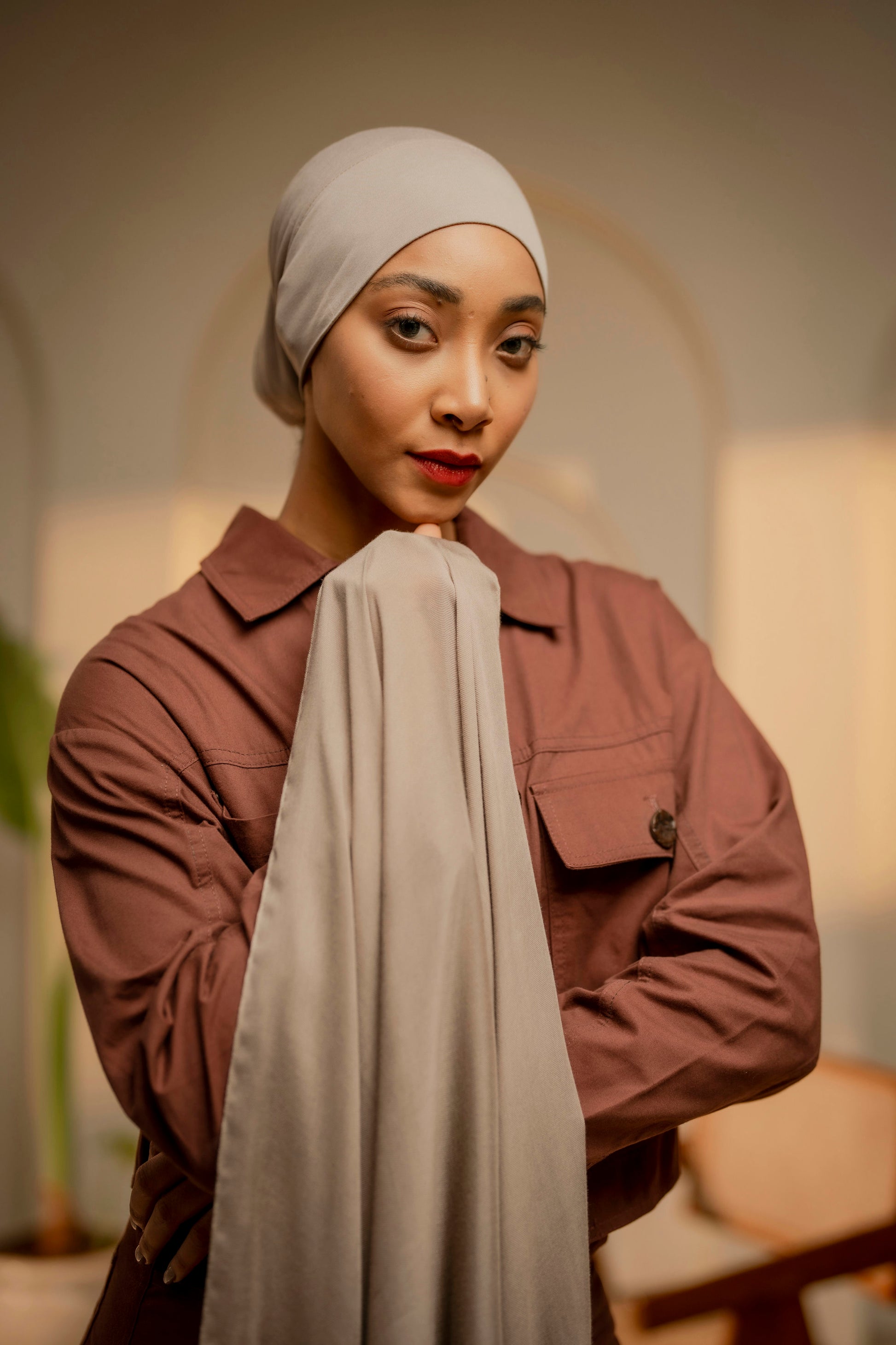 Woman wearing a beige hijab and brown jacket indoors - tan