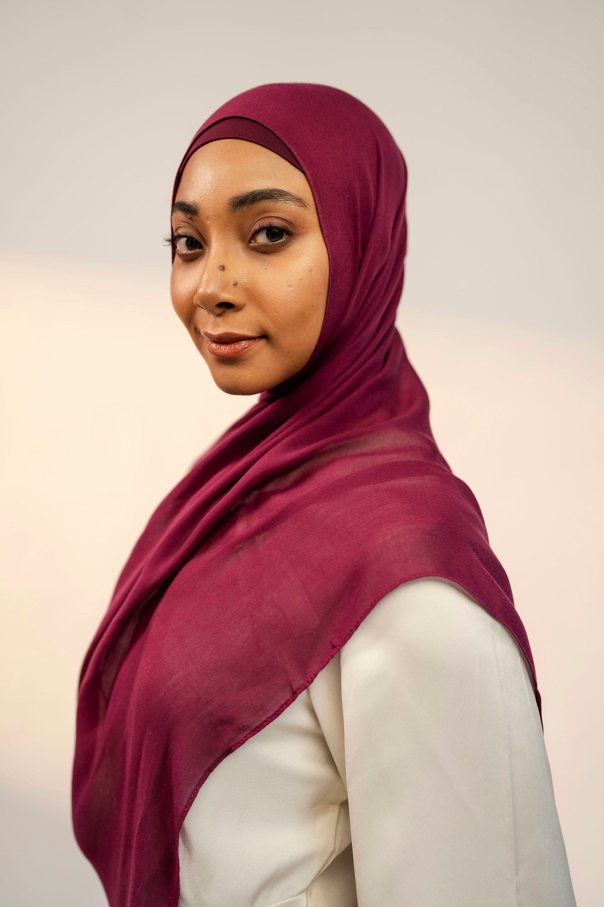 Woman wearing a maroon hijab against a plain background - wine colour