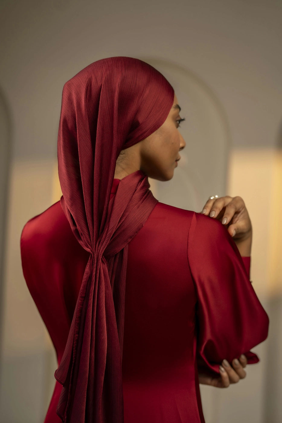 Woman wearing a red hijab and dress against a neutral background