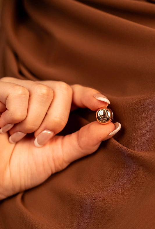 Rose gold hijab magnets on a hand against a brown fabric background