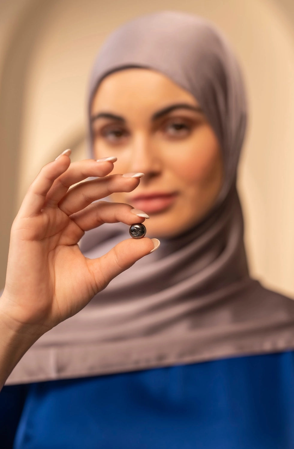 Woman wearing a hijab holding a small silver hijab magnet with a blurred background