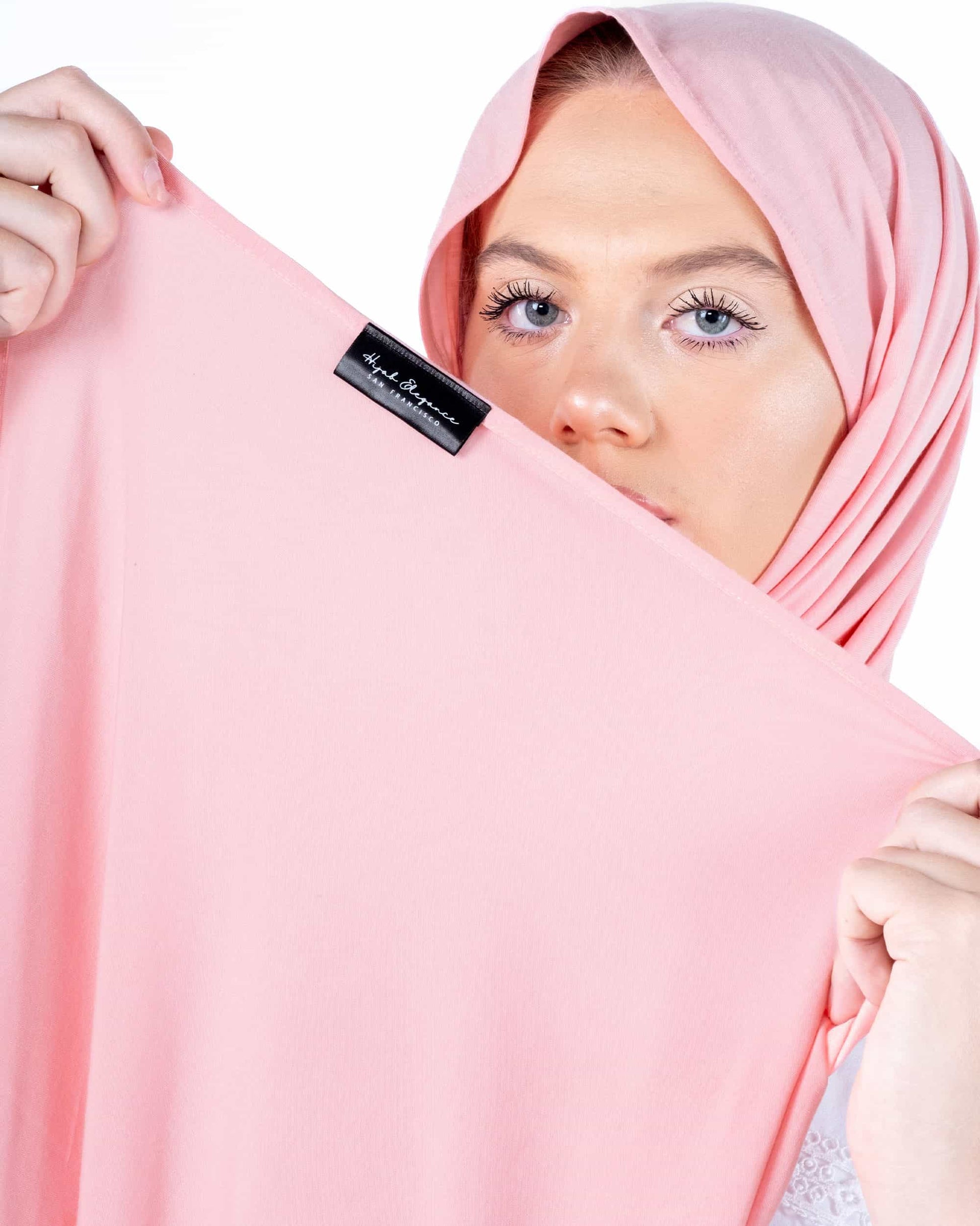 A person holding a pink bamboo and jersey hijab with a visible brand tag.
