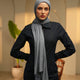 Person wearing a black outfit with a gray scarf and headscarf in an indoor setting.