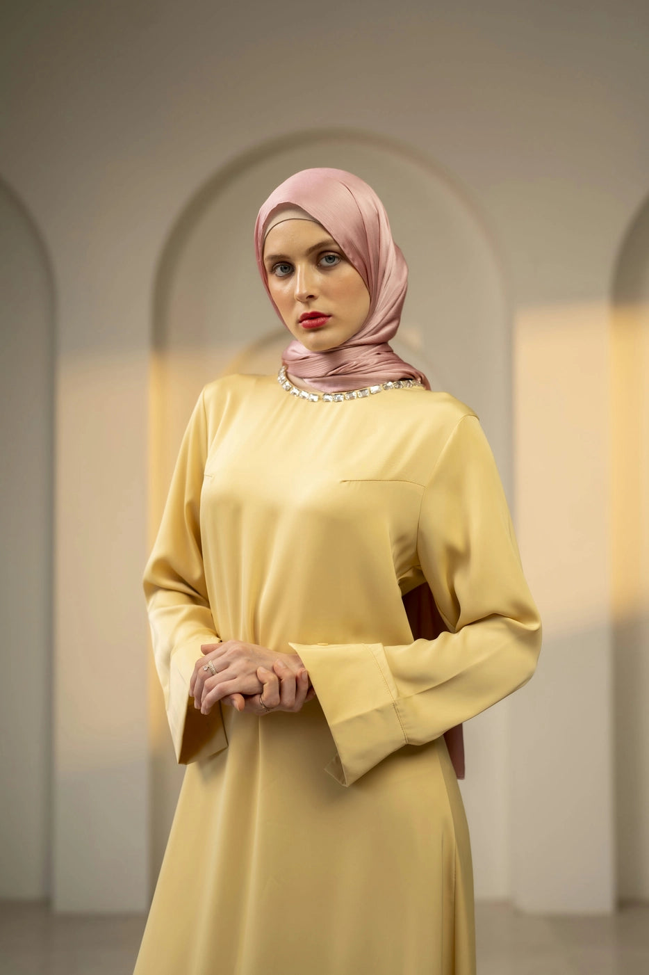 Woman wearing a yellow dress and pink hijab in an archway setting