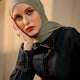 Woman wearing a green hijab with a blurred background resting her face on her palm